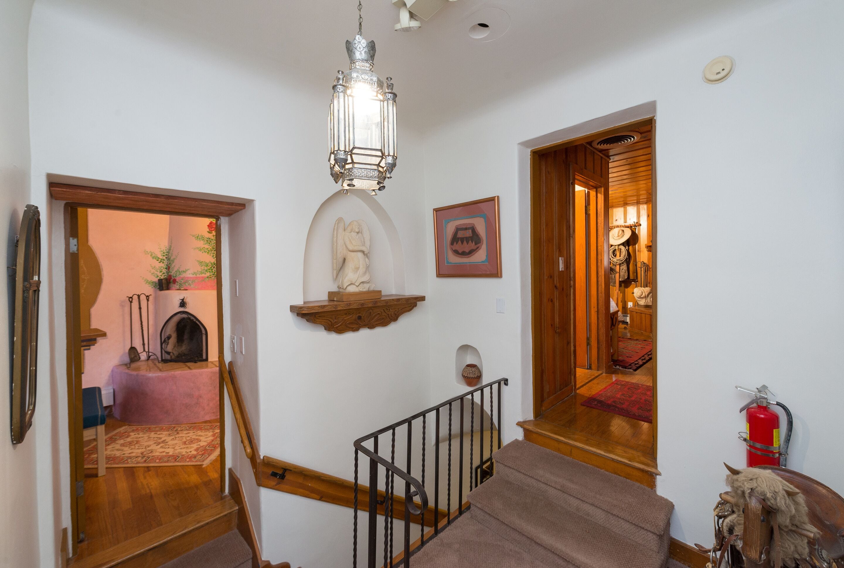 A staircase with a wooden handrail, a hanging lantern, and a small statue on the wall.