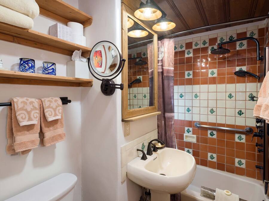 A bathroom with a sink, mirror, shelf with towels, and a shower area.