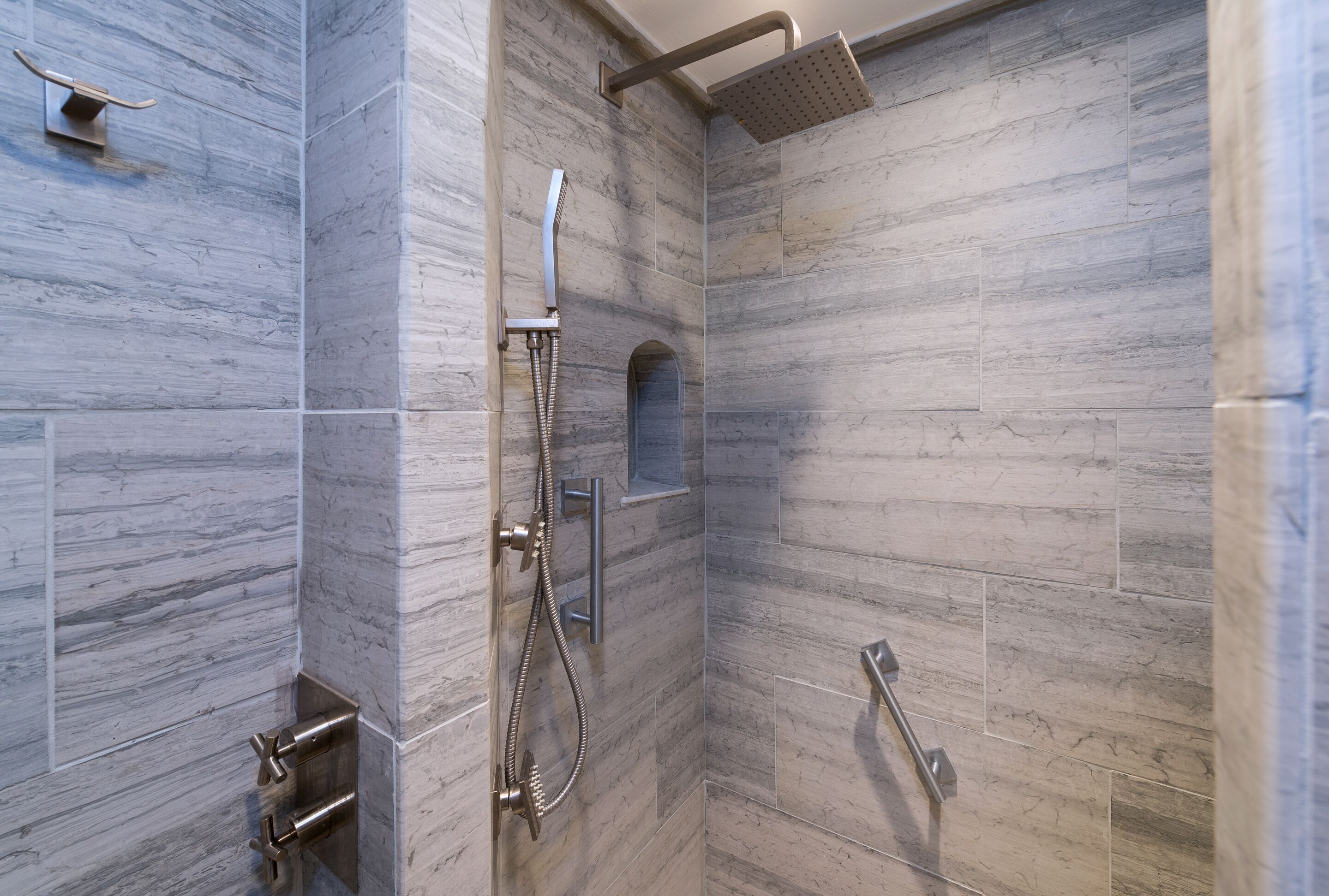 A modern shower area with a handheld showerhead, a fixed showerhead, and a handheld shower hose.