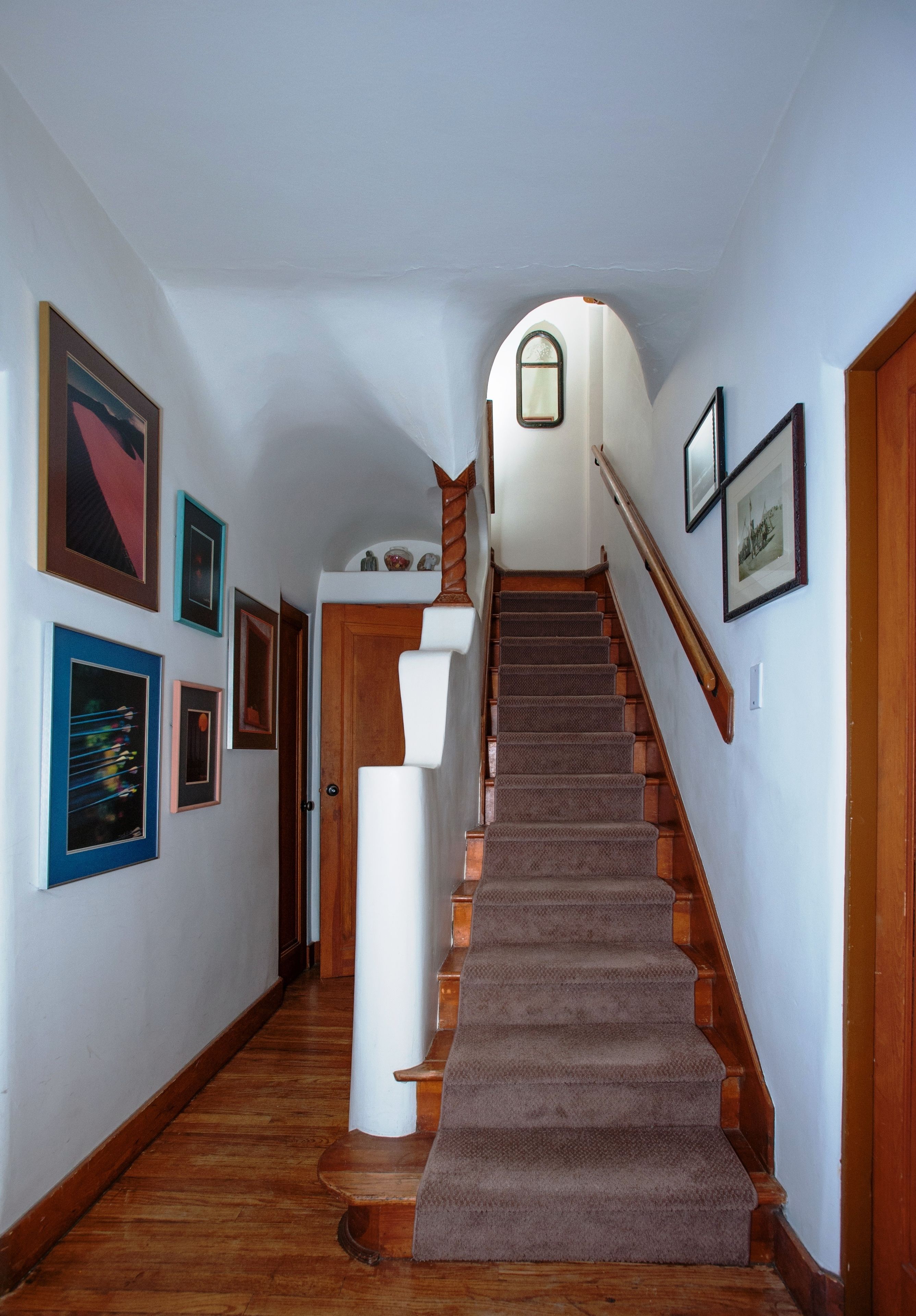 A hallway with a wooden staircase, framed pictures on the walls, and a white door at the top.