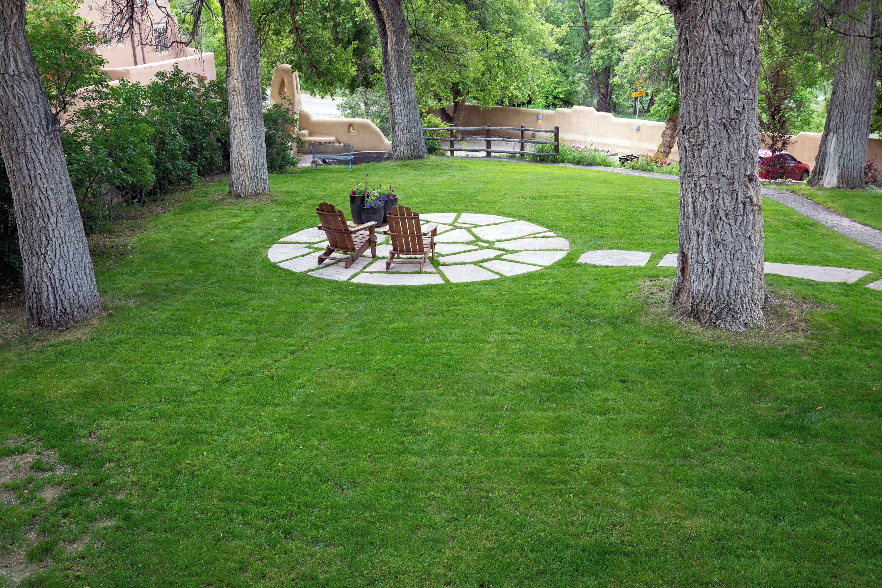A well-maintained lawn with two Adirondack chairs and a circular stone pattern.