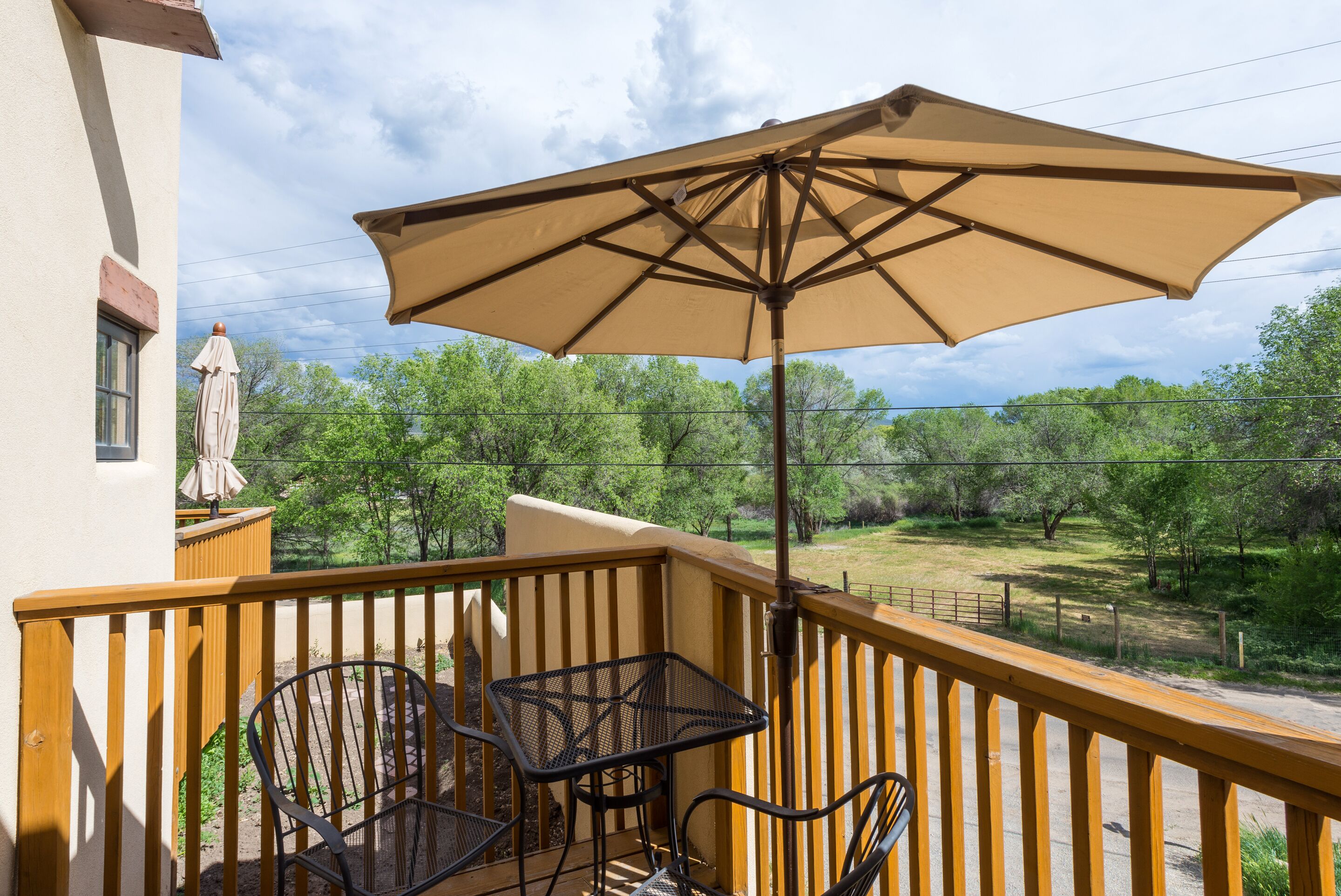 Un balcon avec une table et des chaises, un grand parasol et une vue sur un paysage verdoyant.