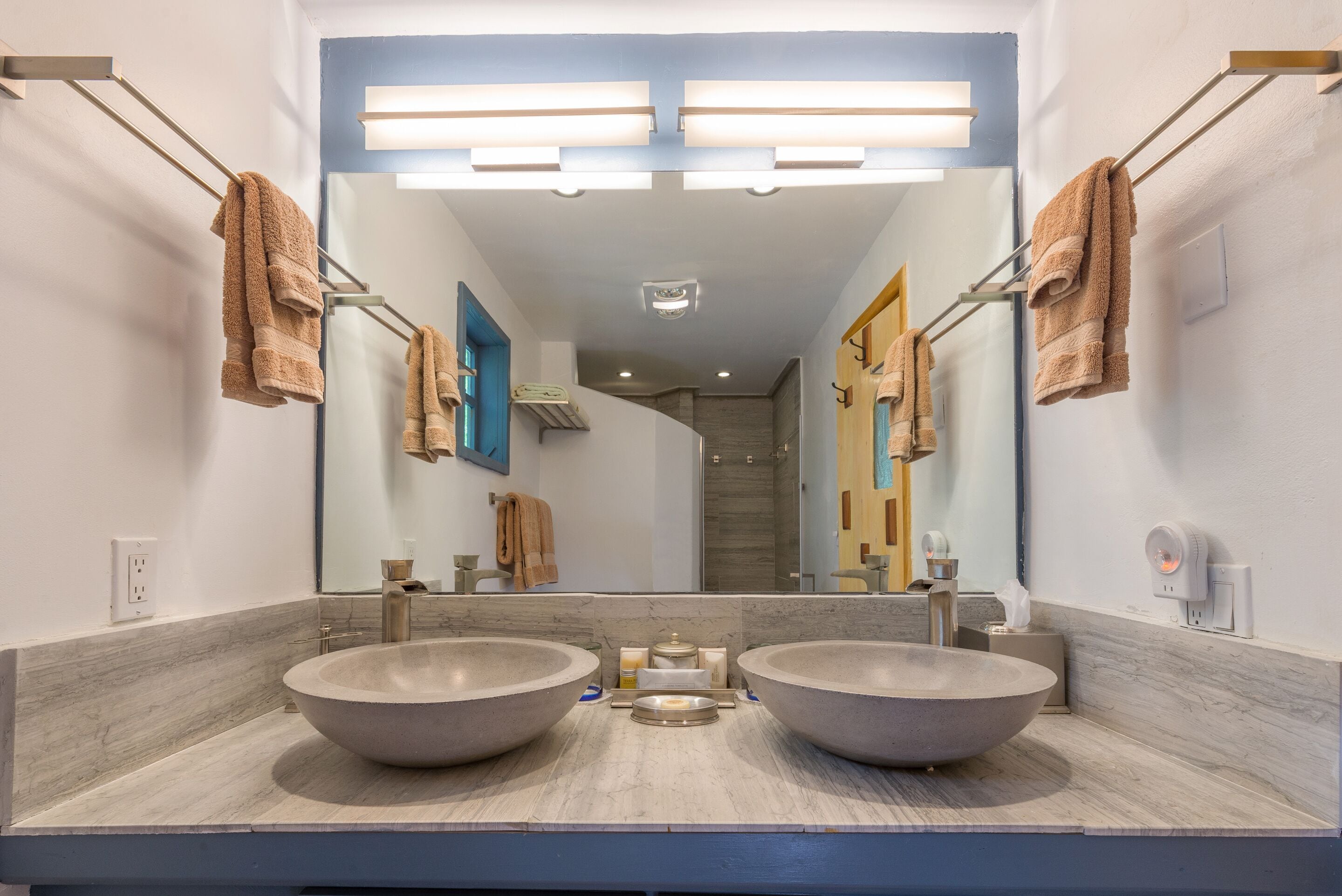A modern bathroom with two large sinks, a mirror, and overhead lighting.