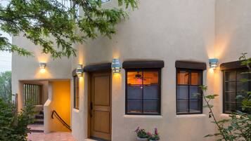 A stucco building with a wooden front door, multiple windows with shutters, and outdoor potted plants.