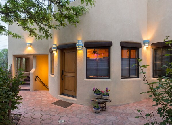 A stucco building with a wooden front door, multiple windows with shutters, and outdoor potted plants. - Inn on La Loma Plaza (Taos)