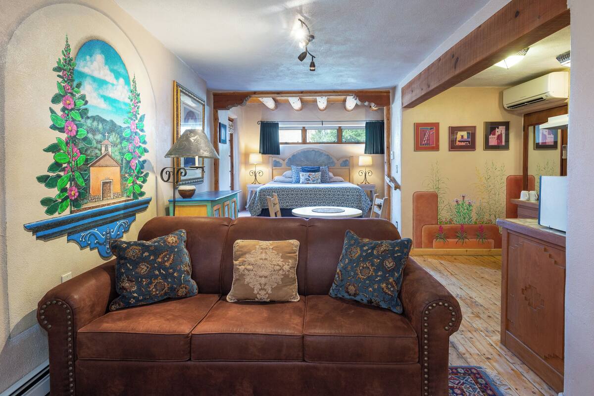 A cozy living room with a brown leather sofa, a dining area with a table and chairs, and a kitchen area with wooden cabinets.
