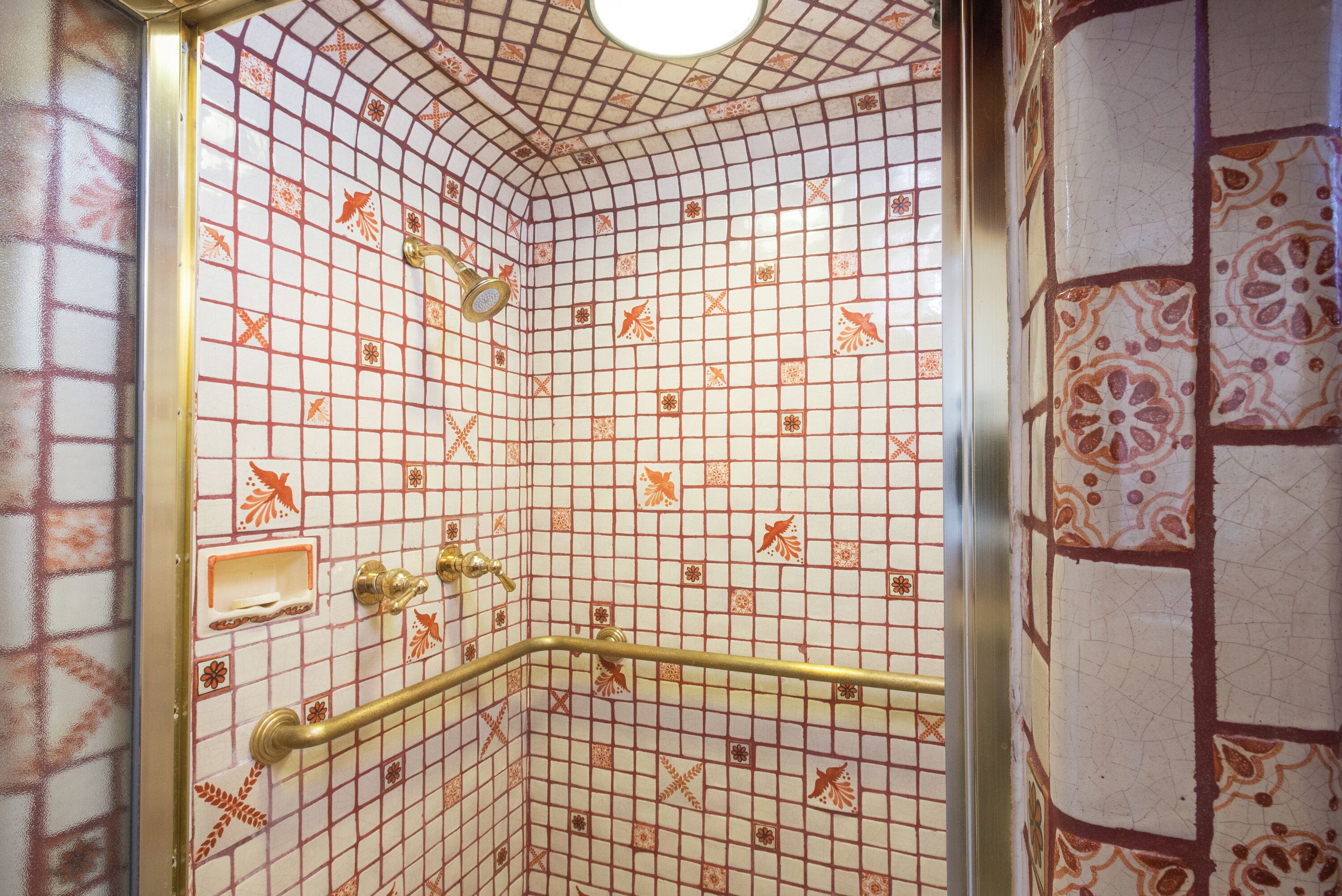 A bathroom with a tiled floor and walls, a shower area with a glass door, and a handrail.