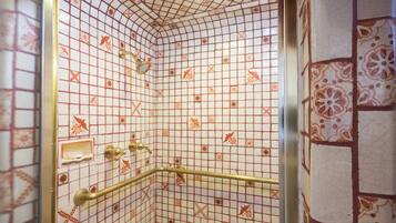 A bathroom with a tiled floor and walls, a shower area with a glass door, and a handrail.