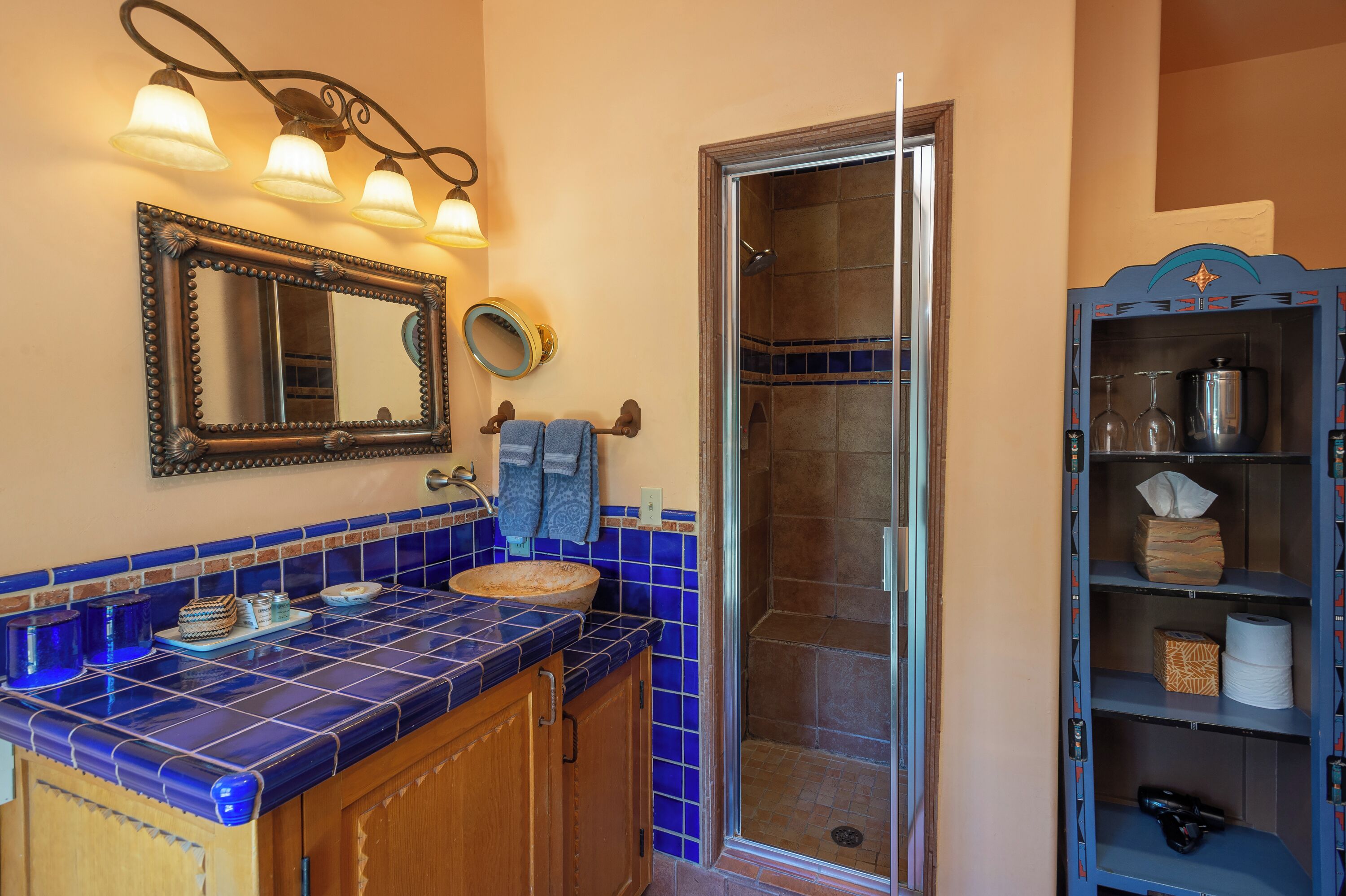 A bathroom with a blue-tiled vanity, a large mirror, and a shower enclosure.