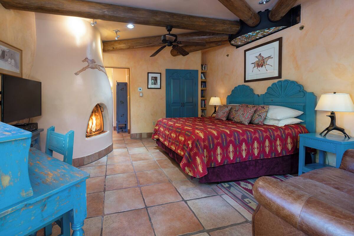 A bedroom with a bed, a television, a fireplace, and a ceiling fan.