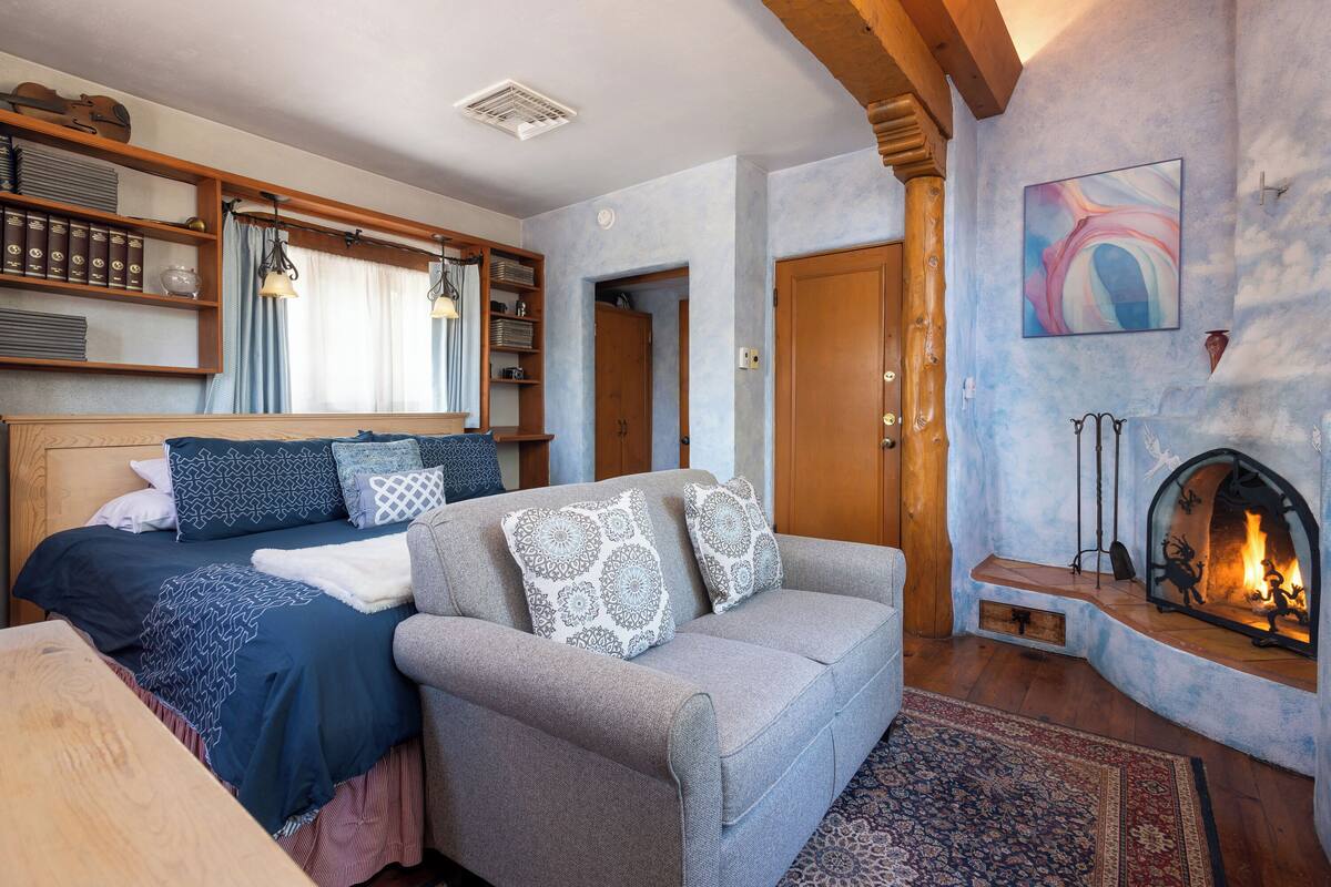 A cozy room with a bed, a sofa, a fireplace, and a bookshelf.