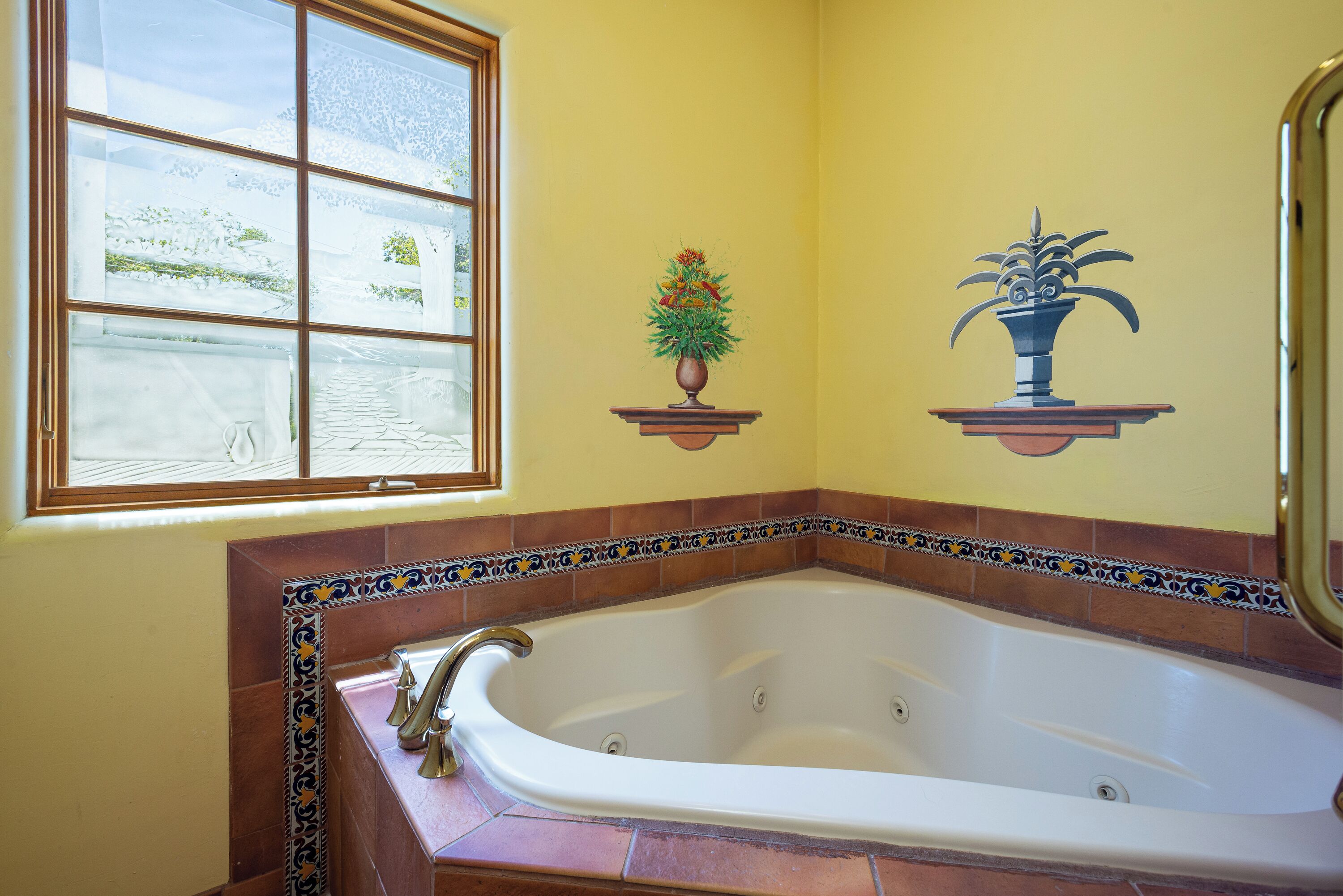 A bathroom with a large bathtub, a window with a view of a snowy landscape, and decorative wall tiles.