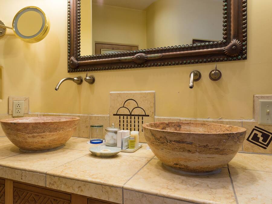 Un bagno con due ampi lavabi in pietra, uno specchio e un portascopevoli.