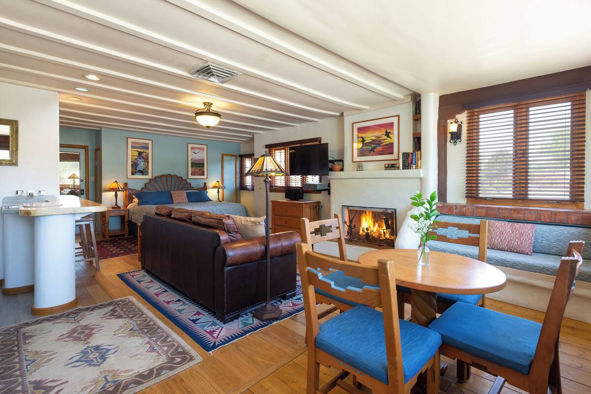 A cozy living room with a fireplace, a dining area with a wooden table and chairs, a sofa, and a TV mounted on the wall.