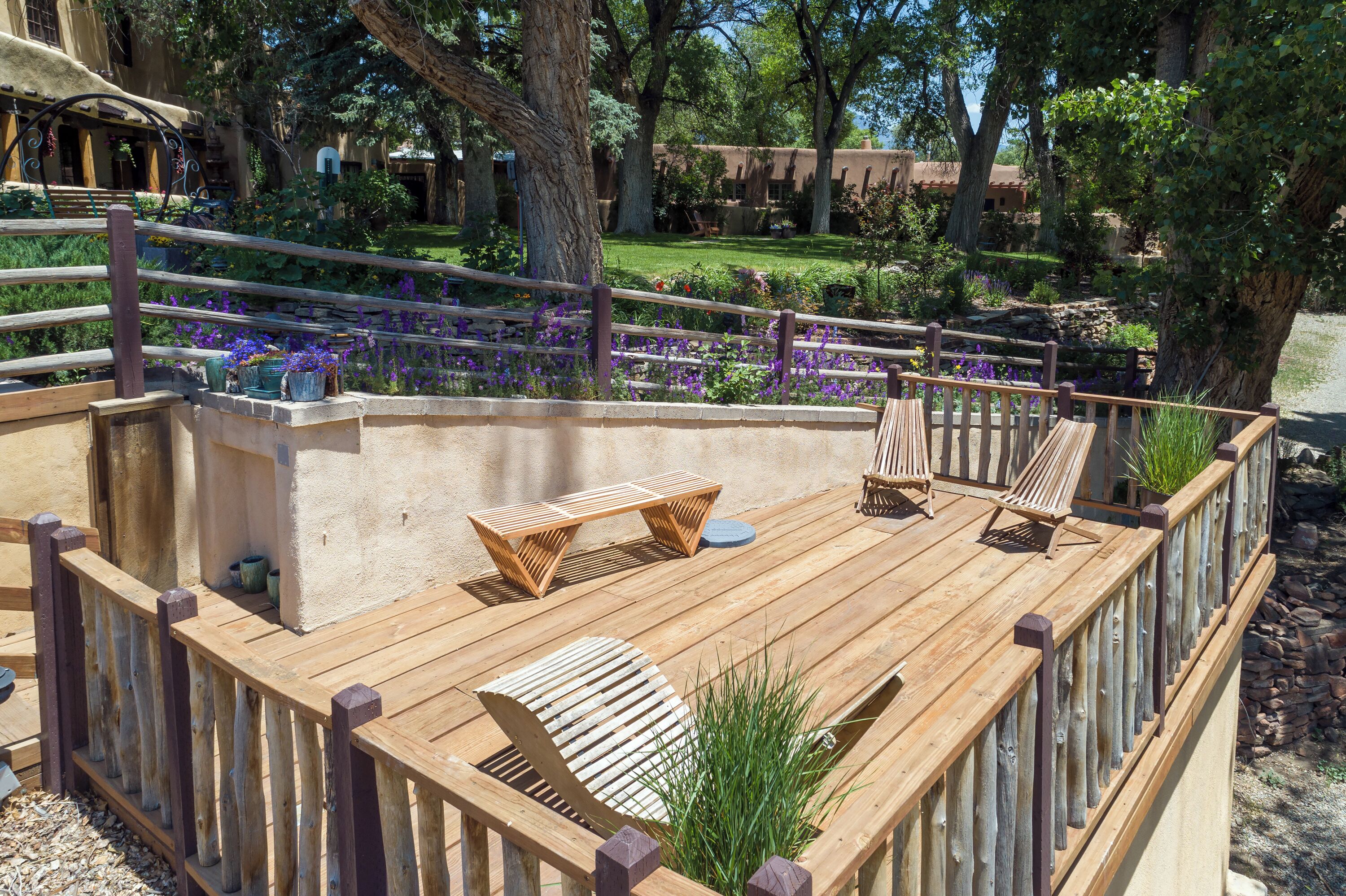A wooden deck with seating, surrounded by a wooden fence and a garden with purple flowers.