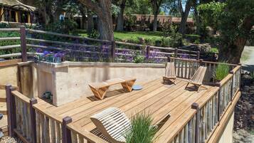 A wooden deck with seating, surrounded by a wooden fence and a garden with purple flowers.