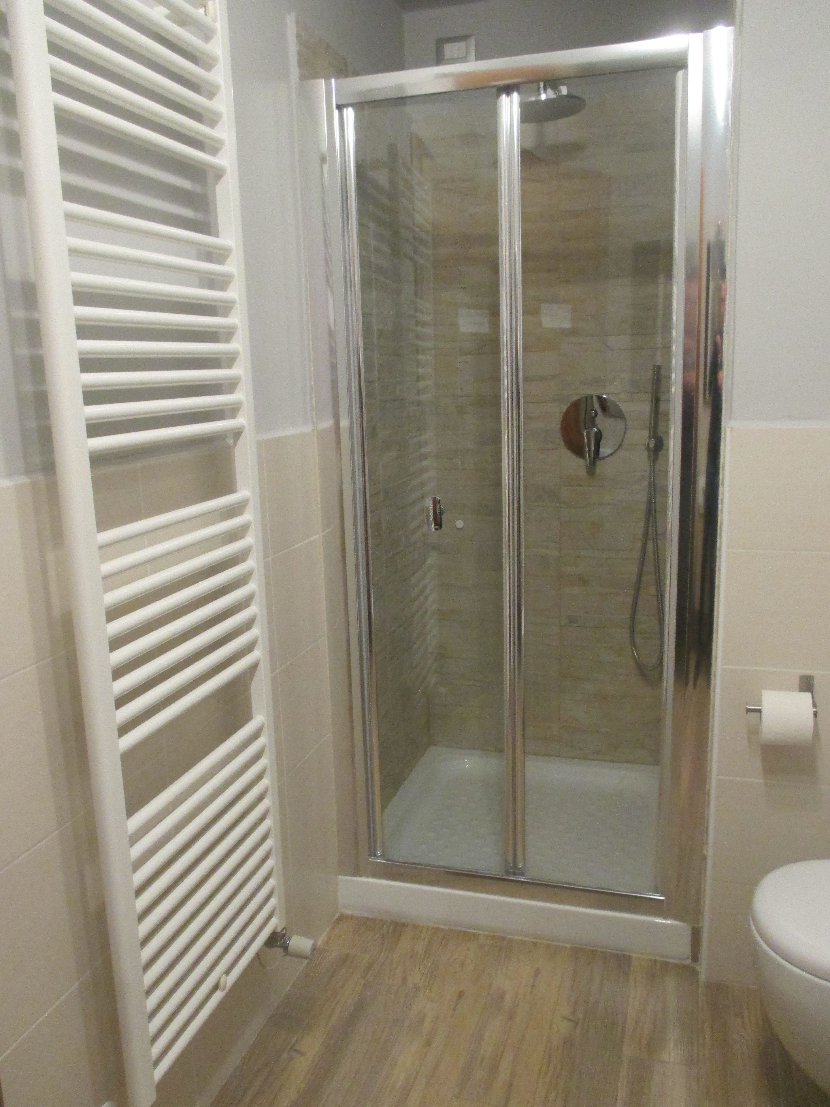 A modern bathroom with a glass-enclosed shower, white tiled walls, and a wooden floor.