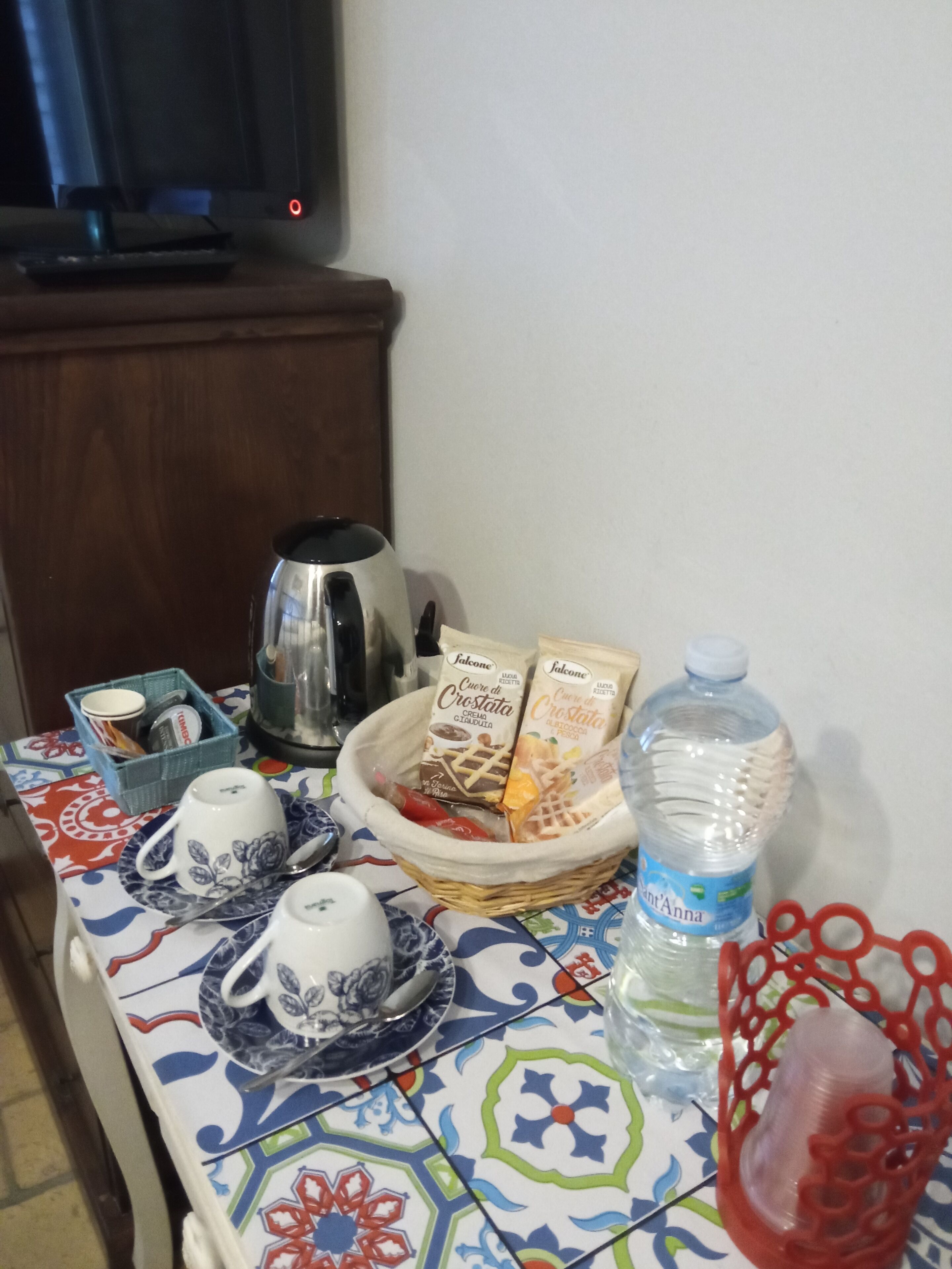 A table with a coffee maker, a basket of food items, a water bottle, and a decorative red basket.