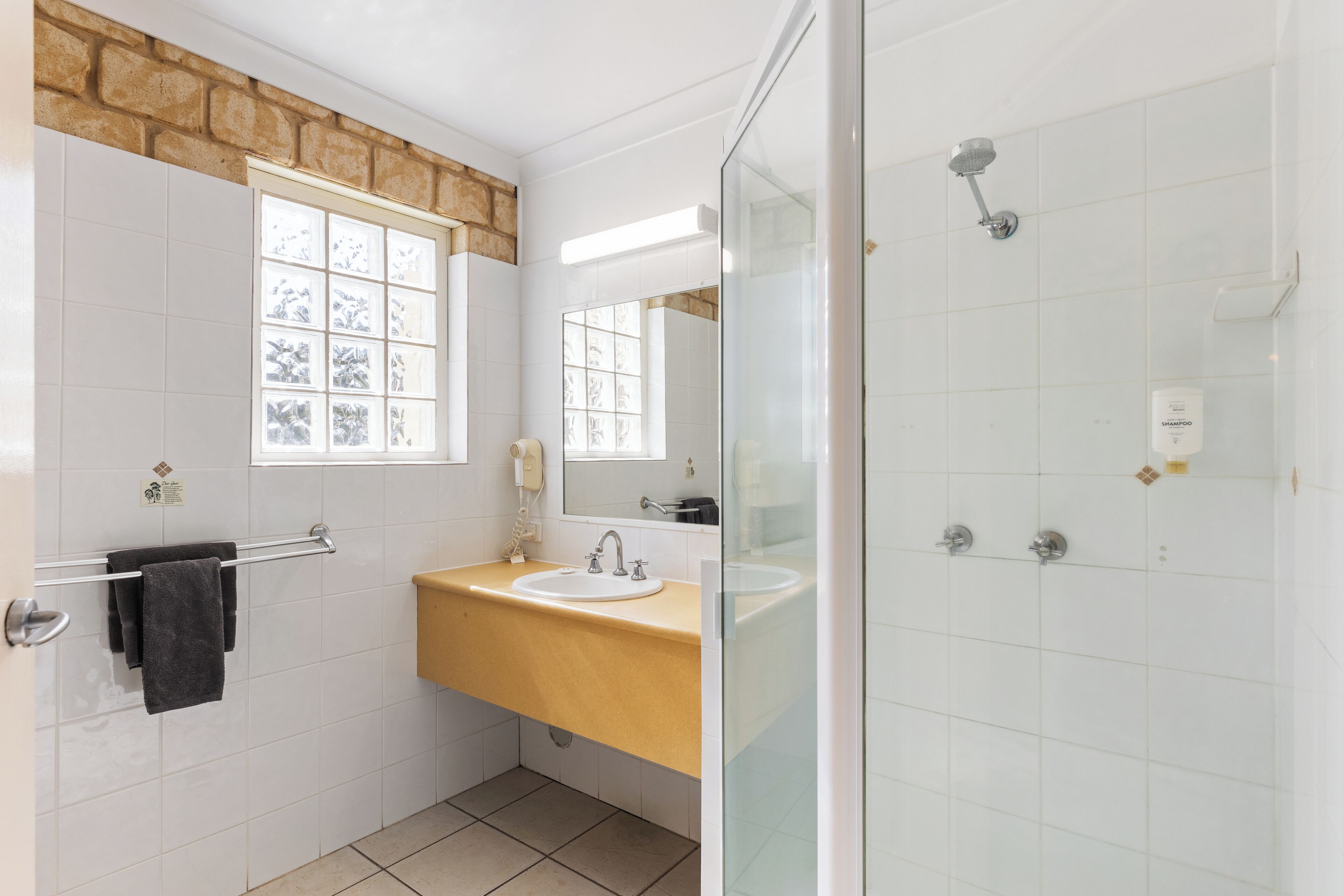 A bathroom with a beige countertop sink, a glass shower enclosure, and a window with a view of trees.