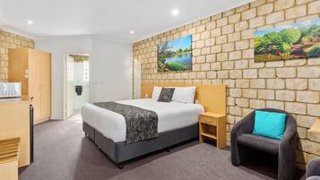 Hotelkamer met een groot bed, een stoel, een bureau en een stenen muur met twee schilderijen.