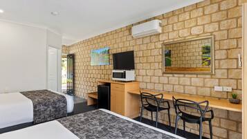 A hotel room with two beds, a desk, a chair, a TV, and a stone wall.