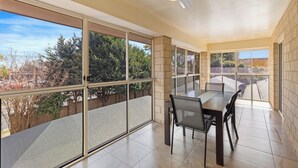 A spacious balcony with a dining table and chairs, large windows offering a view of trees and buildings, and a ceiling fan. - Great Divide Motor Inn (East Toowoomba)
