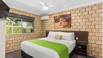 Una camera da letto con una parete a mattoni, un letto con copripiumino verde e bianco, un comodino e una ventola a soffitto.