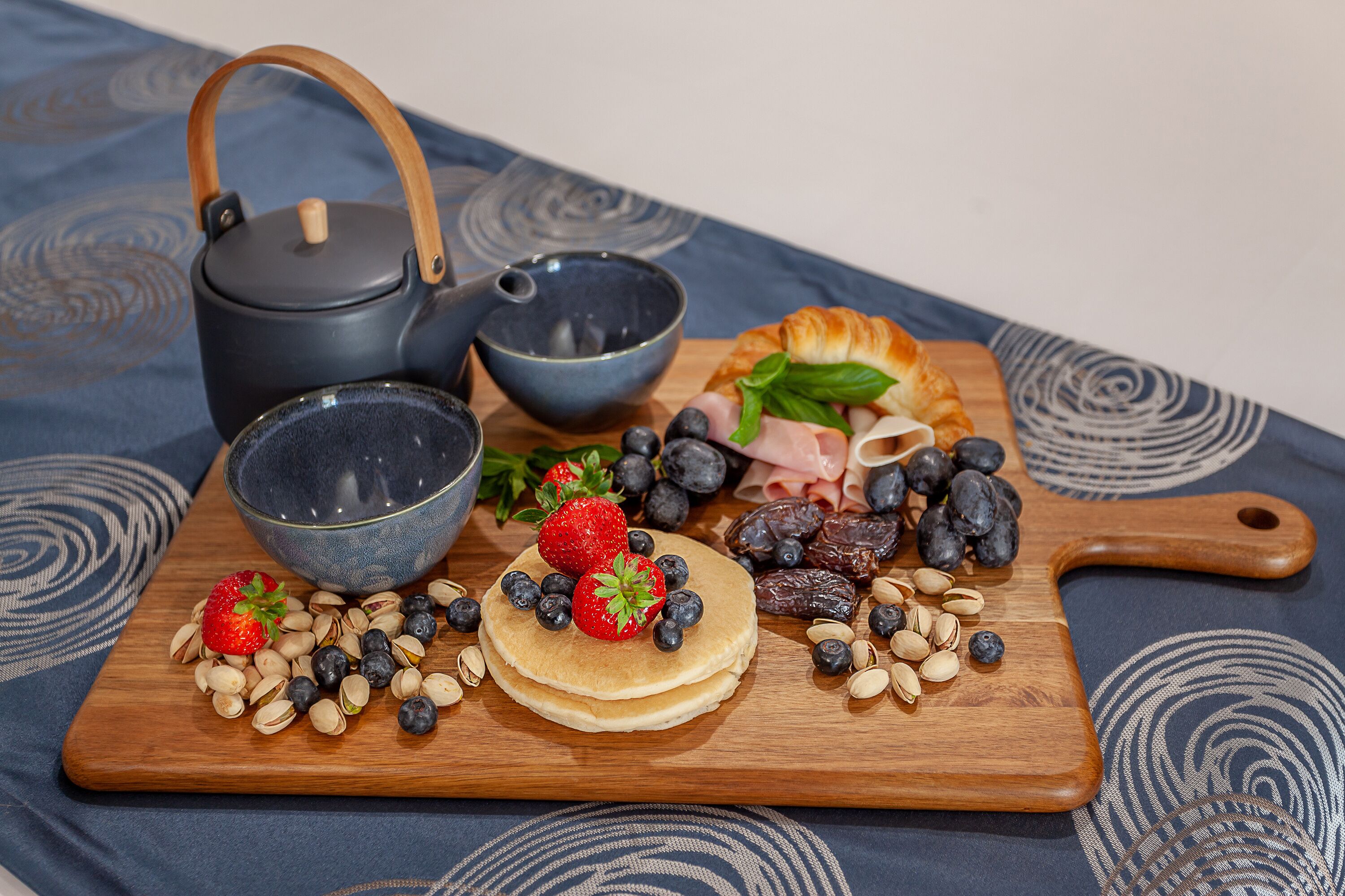 A wooden board with pancakes, strawberries, blueberries, dates, and almonds.