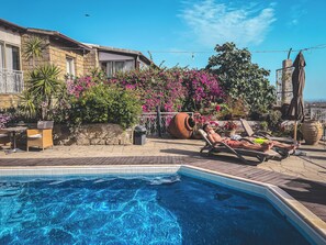 A pool area with lounge chairs, a stone building, and vibrant pink flowers.