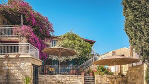 Zwembadgedeelte met stenen muren, twee parasols en een trap naar een balkon met roze bloemen.