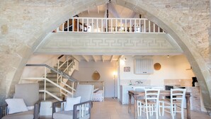 Een ruime woonkamer met een hoge plafond, stenen muren, een balkon en een keukenhoek.