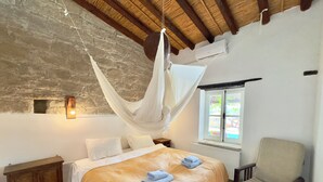 Een slaapkamer met een bed, een stoel, een nachtkastje, een raam en een stenen muur.