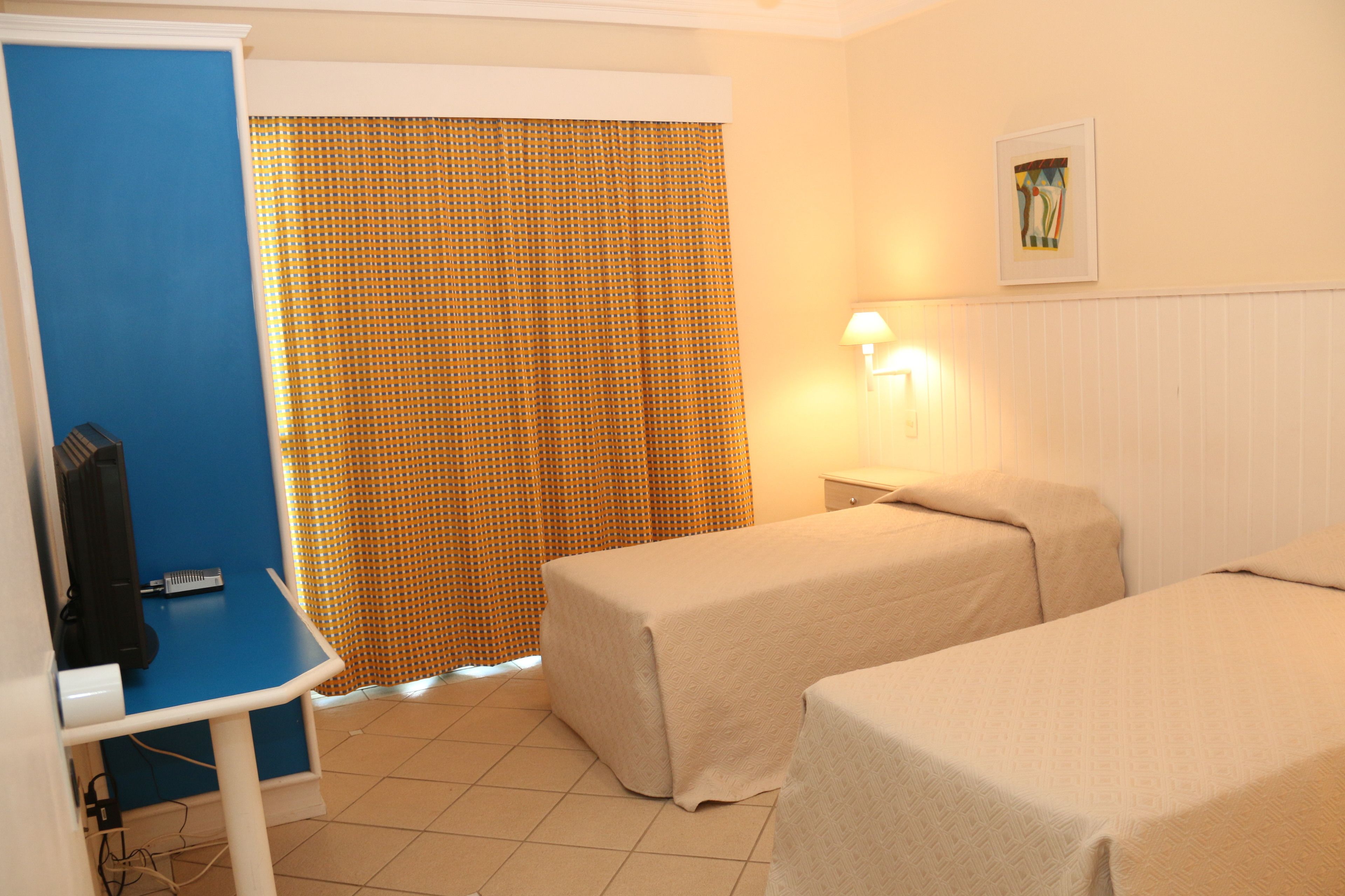 A hotel room with two beds, a desk, a television, and a curtain.