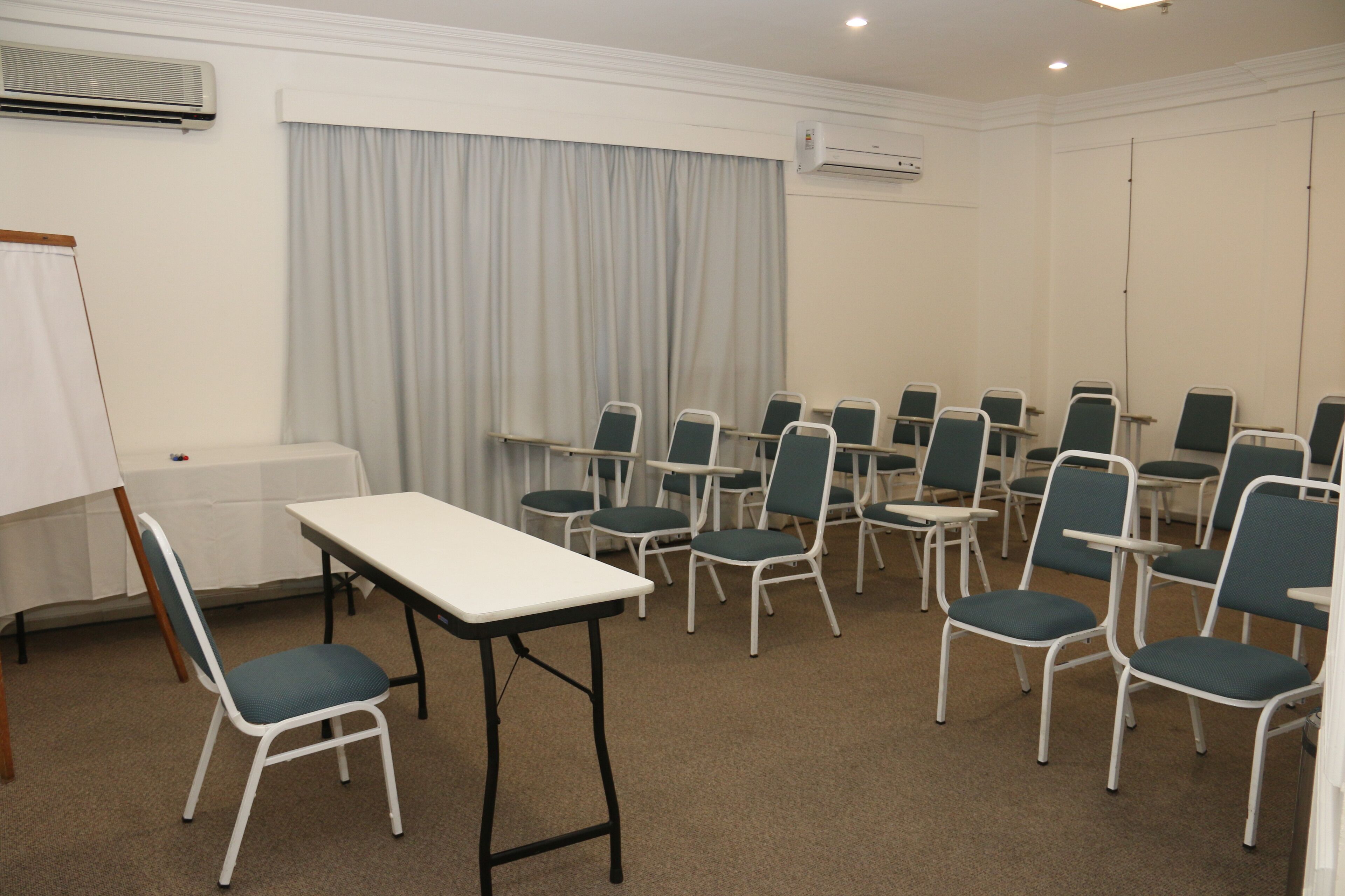 Una sala de conferencias con una mesa blanca, varias sillas, una pizarra y un equipo de aire acondicionado.