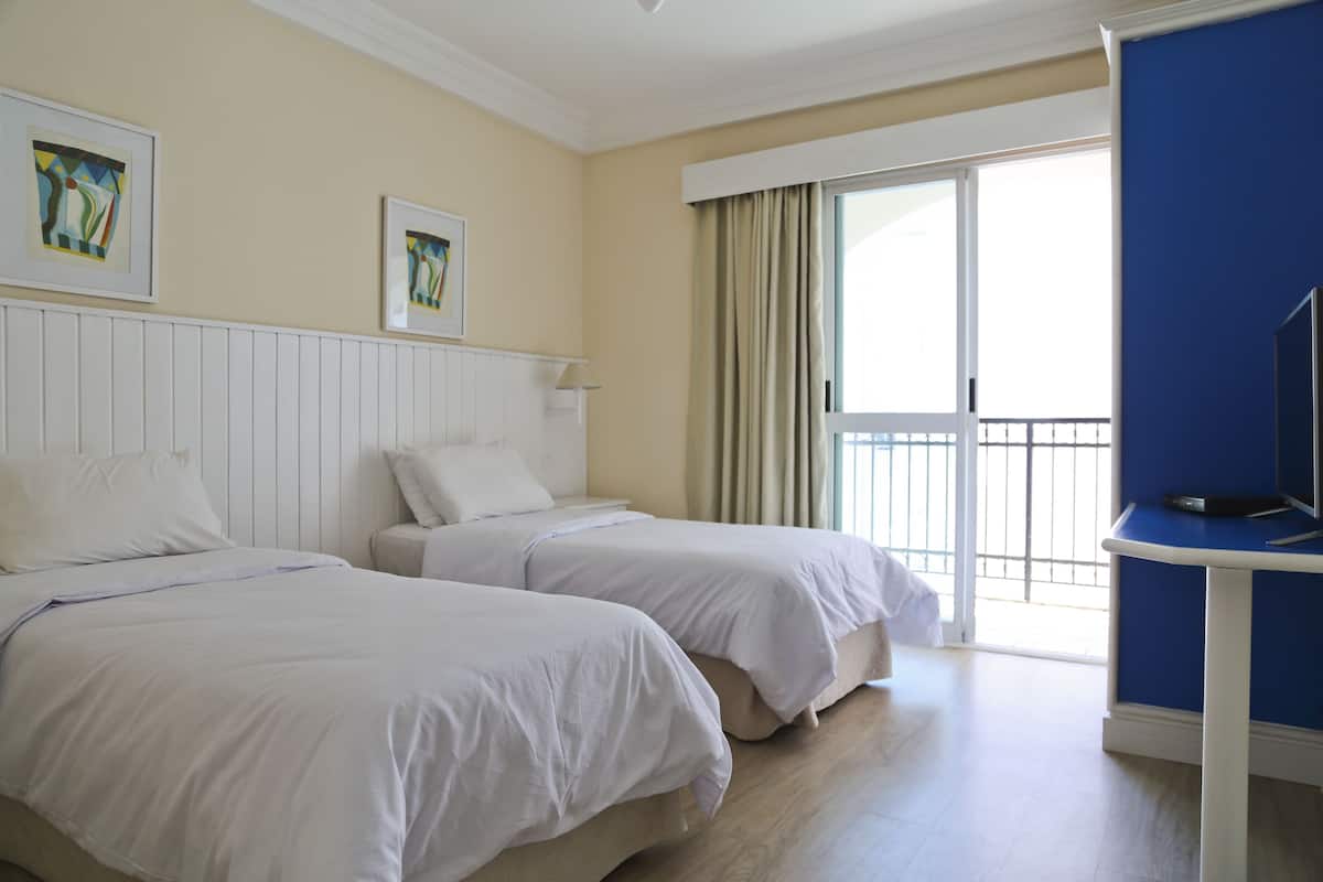Een hotelkamer met twee bedden, een televisie en een balkon met gordijnen.