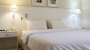 Une chambre d’hôtel comprenant un lit, des lampes de chevet, une table de chevet avec un téléphone et deux œuvres d’art encadrées accrochées au mur.