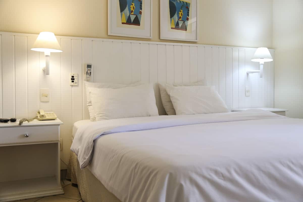 Een hotelkamer met een bed, bedlampen, een nachtkastje met een telefoon en twee ingelijste kunstwerken aan de muur.