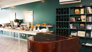 Un coin repas avec une longue table dressée pour le petit-déjeuner, un meuble à vin et une bibliothèque remplie de livres et de récompenses.