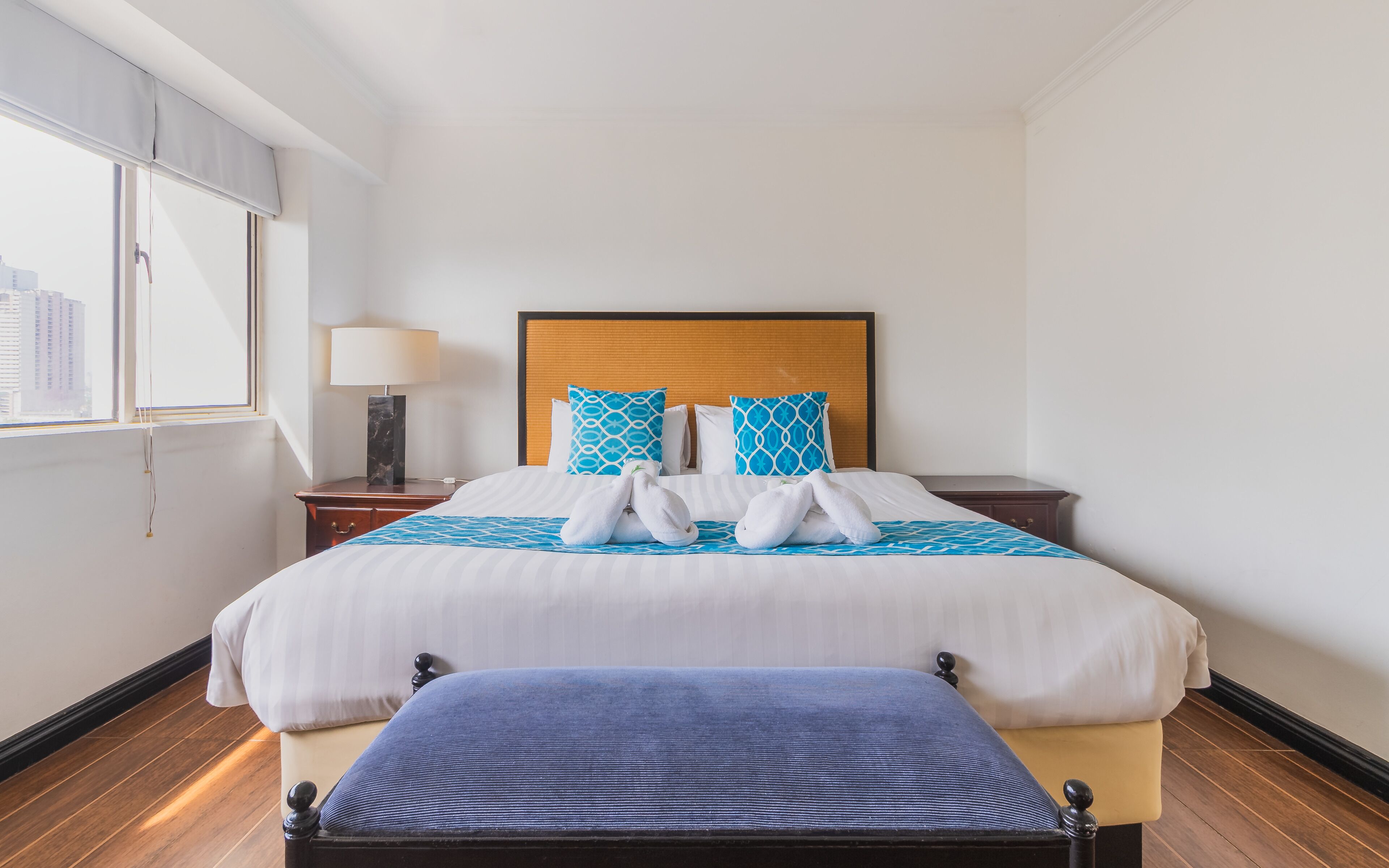 A hotel room with a bed, a nightstand, a lamp, and a window with blinds.