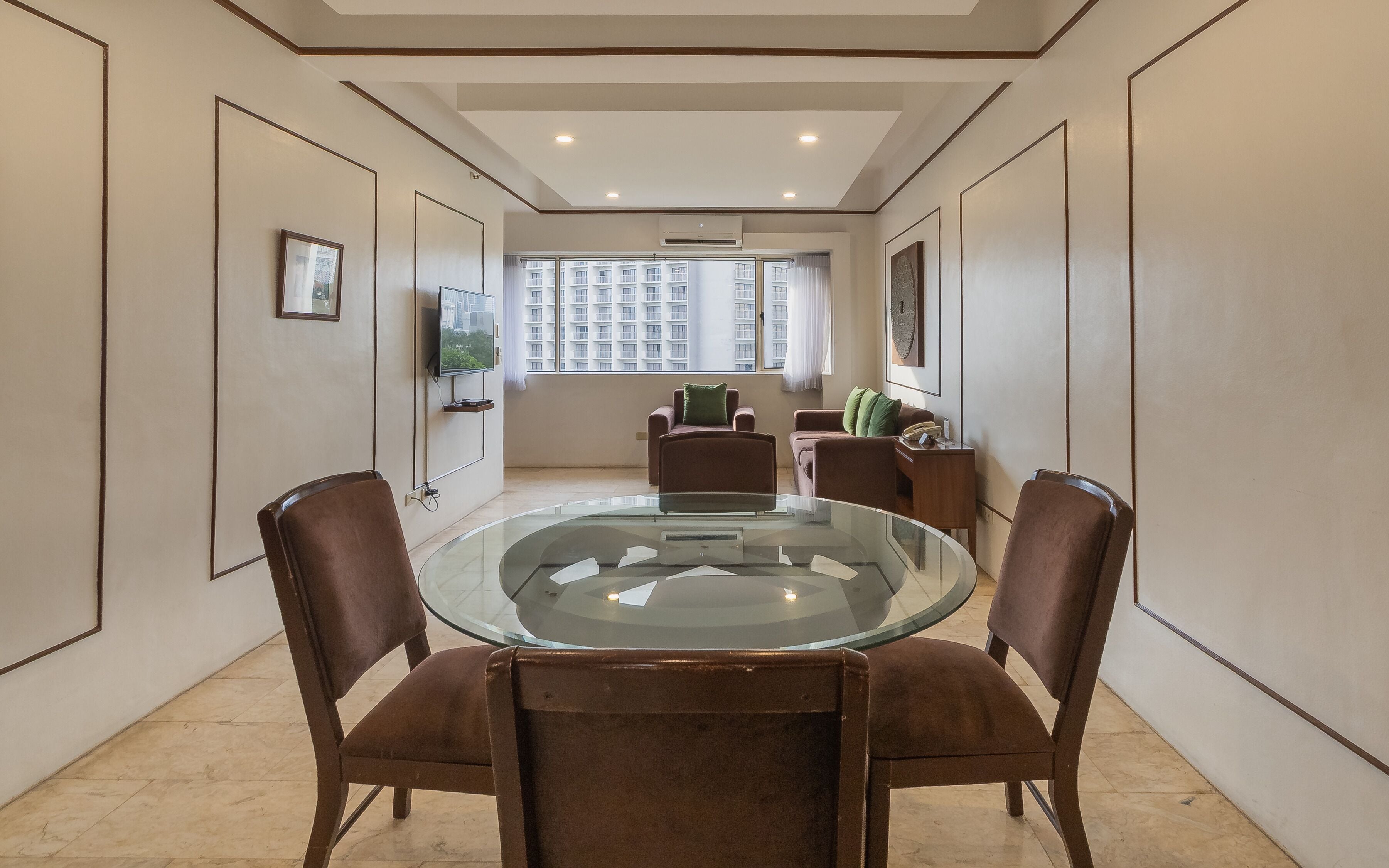 A conference room with a glass table, brown chairs, a television, and a window with a view of high-rise buildings.