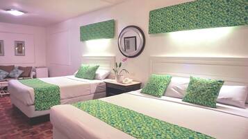 A hotel room with two beds, each with green patterned bedspreads, white pillows, and a bedside table with a lamp and a phone.