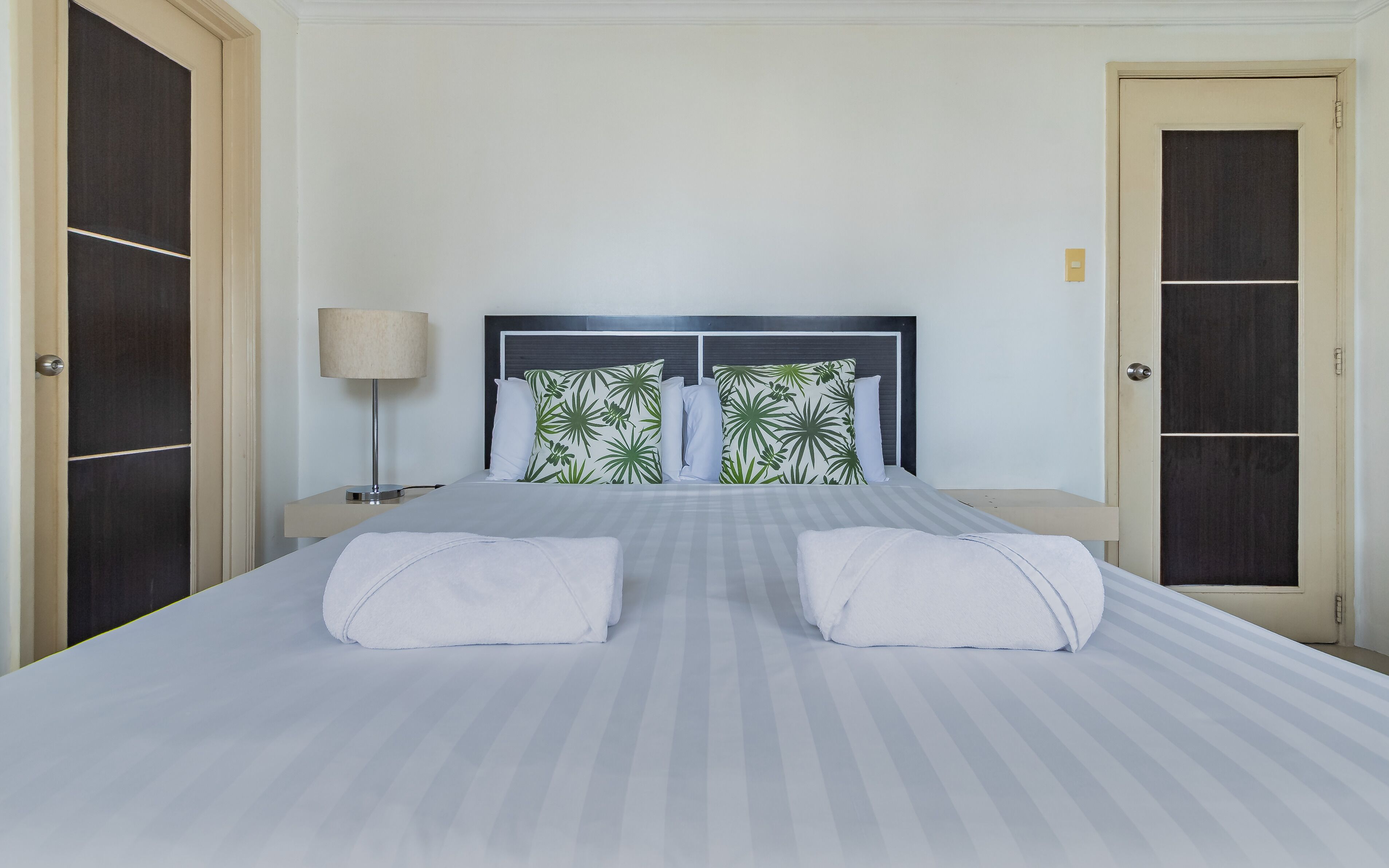 Una habitación de hotel con una cama, dos mesitas de noche, una lámpara y dos puertas.
