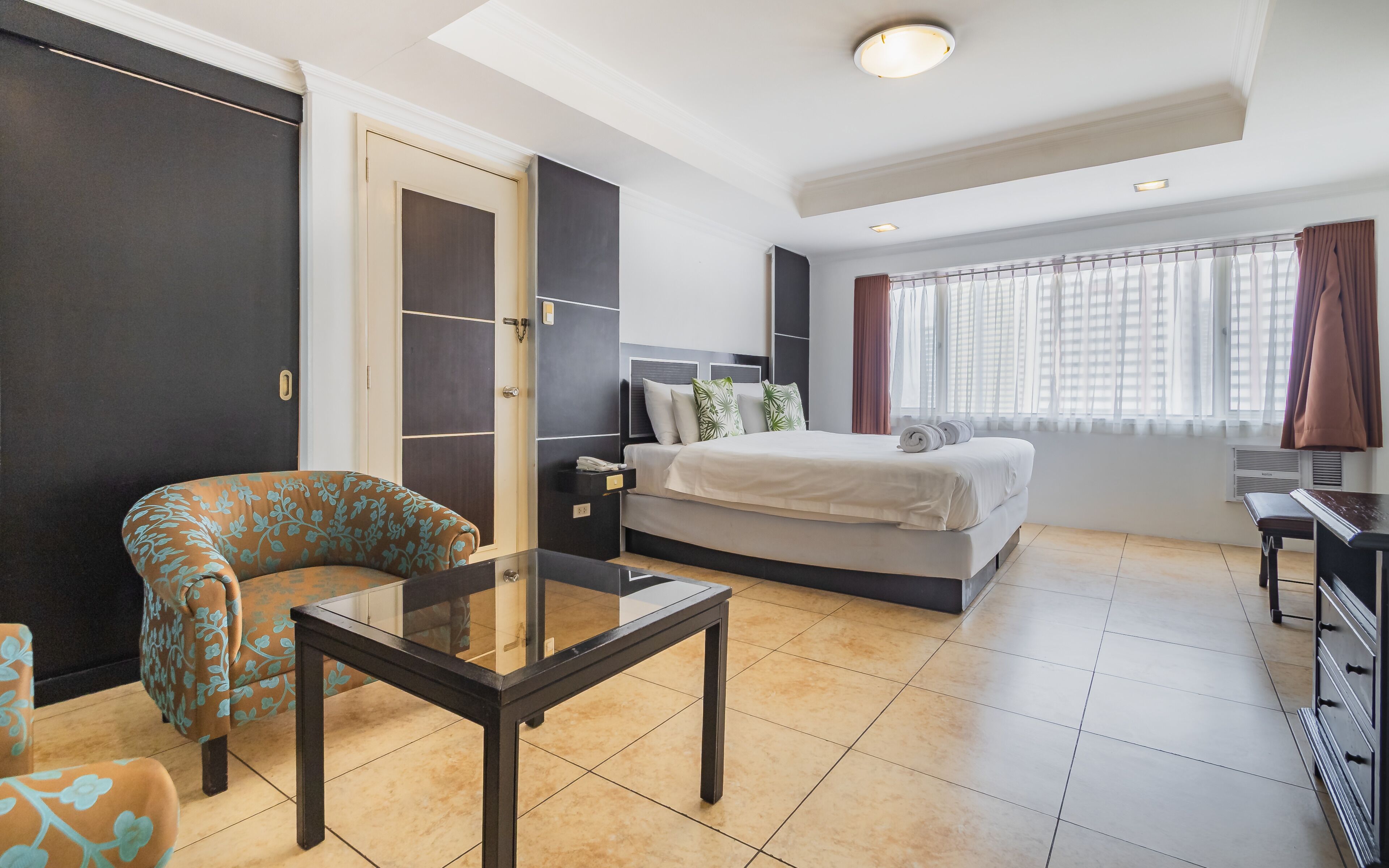Habitación de hotel con cama, mesa de vidrio, una silla, escritorio y armario.