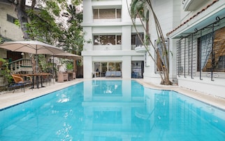 Une piscine à l’eau d’un bleu cristallin, entourée d’un bâtiment blanc doté de balcons et d’un espace extérieur abrité avec des parasols.