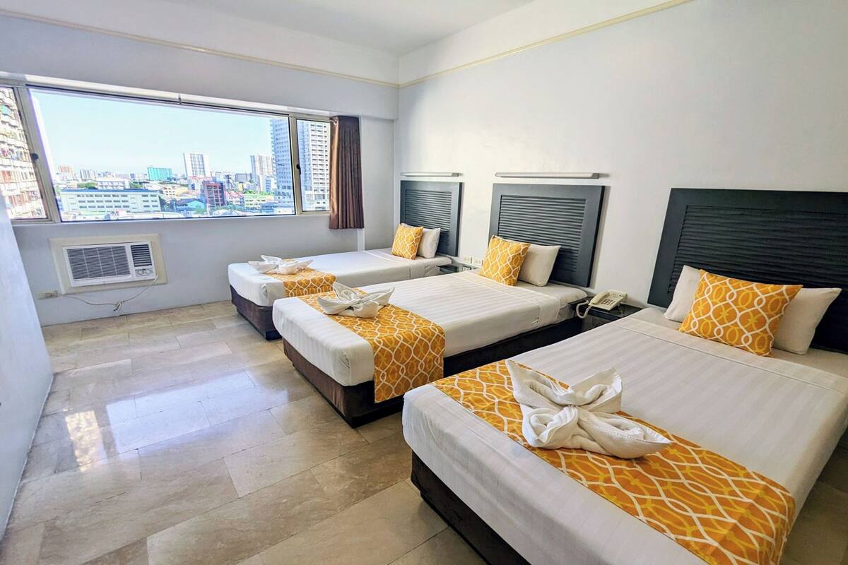 A hotel room with three beds, a large window with a city view, and a modern design.
