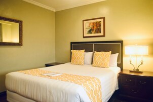 A neatly made bed with a patterned bedspread, a bedside table with a lamp, and a framed picture on the wall.