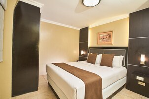A hotel room with a large bed, a headboard with a picture, two bedside lamps, and a door.