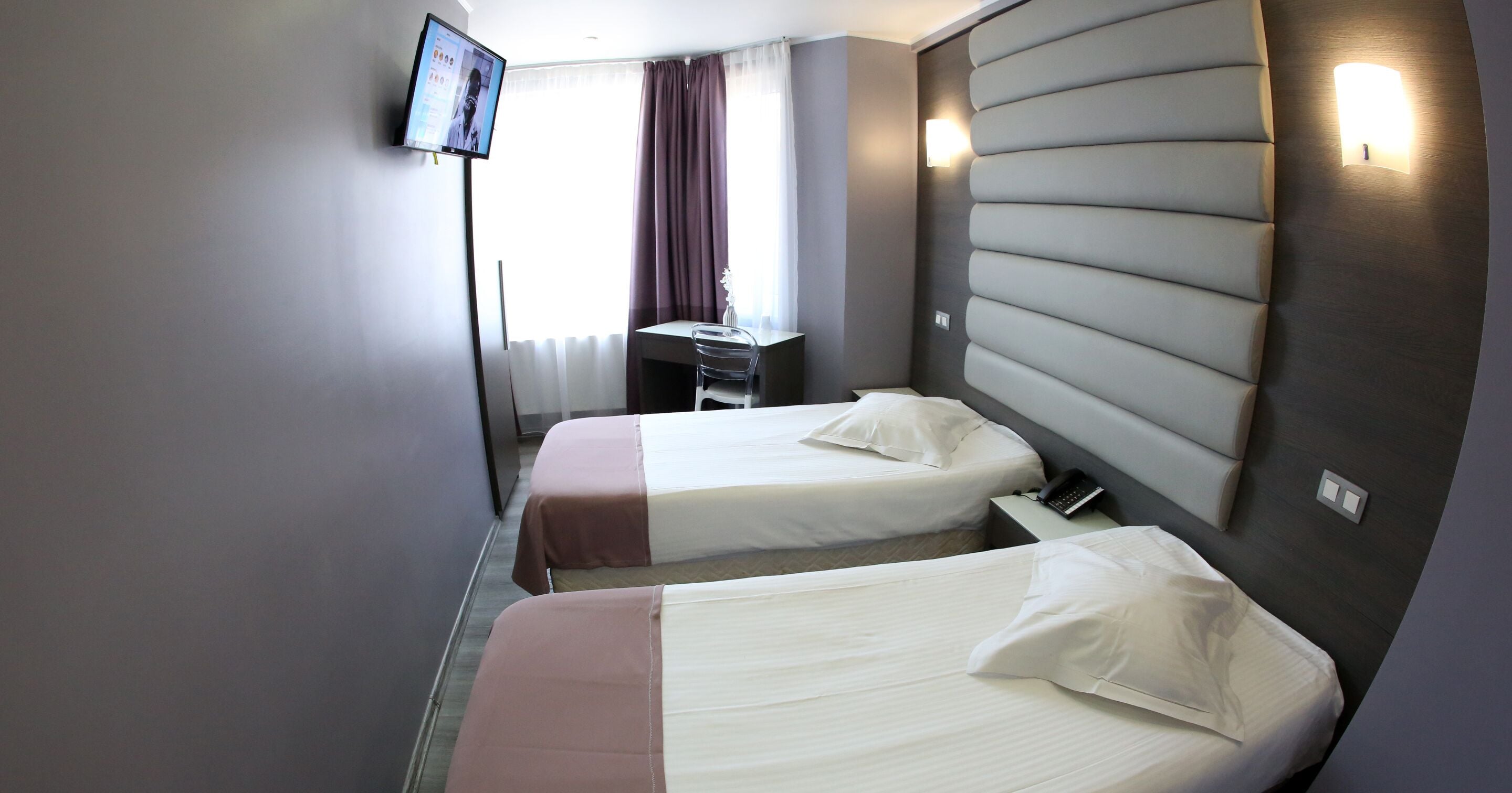 Een hotelkamer met twee bedden, een bureau, een televisie en een raam met gordijnen.