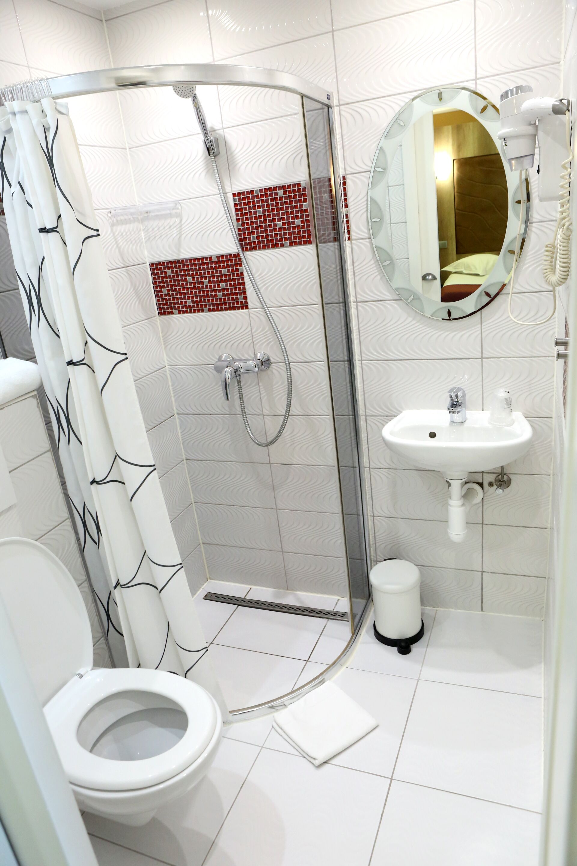 A modern bathroom with a glass-enclosed shower, a white toilet, a sink with a mirror, and a red-tiled accent wall.