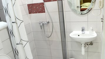 A modern bathroom with a glass-enclosed shower, a white toilet, a sink with a mirror, and a red-tiled accent wall.